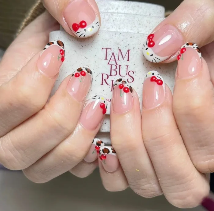 A fun and creative French manicure featuring a playful mashup of Hello Kitty art, cow print, and sweet cherry designs on the tips.