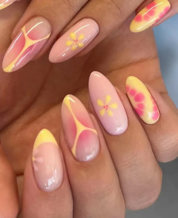 A bright manicure with a mix of butter yellow and pink nails featuring abstract floral patterns and color-blocking.
