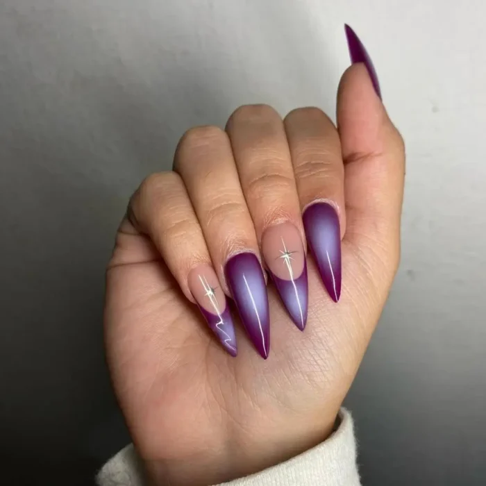 Long stiletto nails with a celestial plum purple nail design, featuring deep luminous purple and silver starburst details.