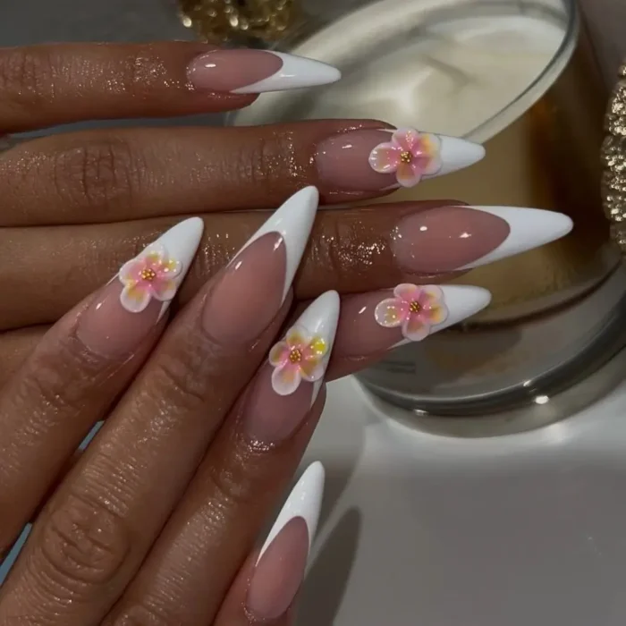 Long stiletto nails with a classic white French manicure, adorned with small 3D pink and yellow flower accents.