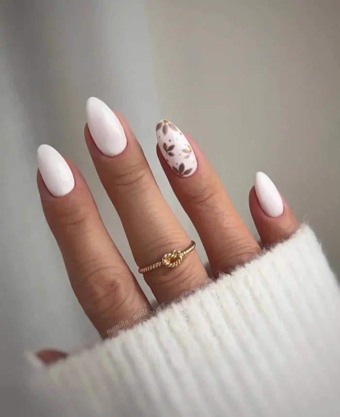 An elegant and modern manicure with crisp white polish and a single accent nail featuring delicate, hand-painted gold botanicals.