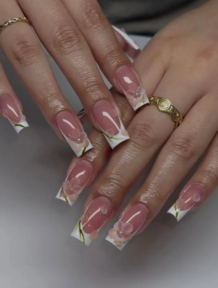 Long square-shaped nails with a classic white French manicure, beautifully embellished with translucent 3D pink flowers featuring gem centers and finely painted green stems and leaves.