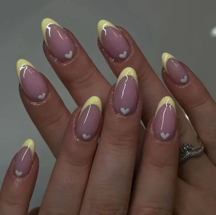 Elegant butter yellow French manicure on almond nails with small white heart details at the base.