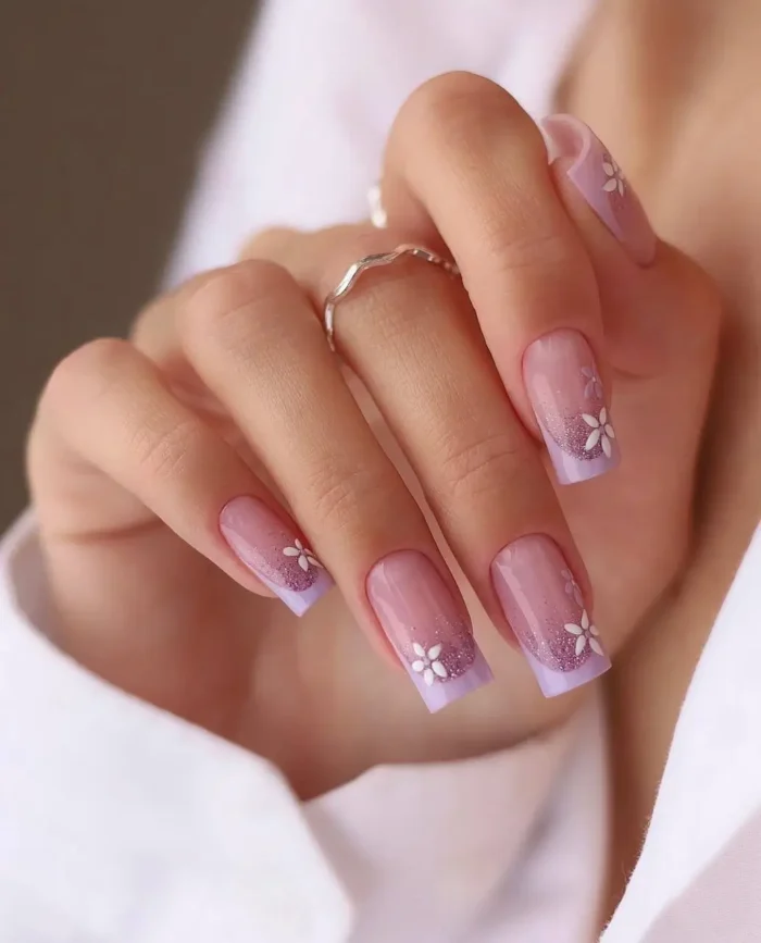 Medium square-shaped nails with a shimmery soft lavender French tip, beautifully accented with small, scattered white stylized flower details.