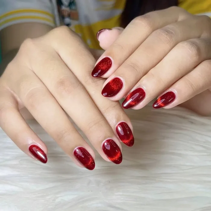 Cute simple gel manicure with a luxurious rich red cat-eye shimmer effect on medium almond-shaped nails.