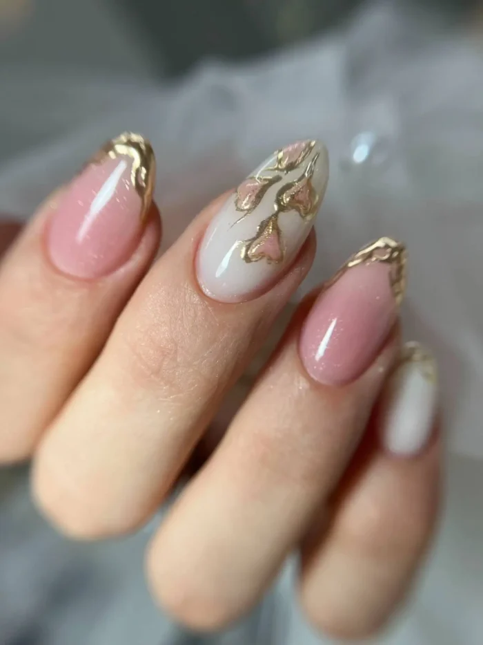 Medium oval/almond nails with a mix of sheer pink and milky white bases, adorned with textured, raised molten gold accents forming French tips and abstract designs.