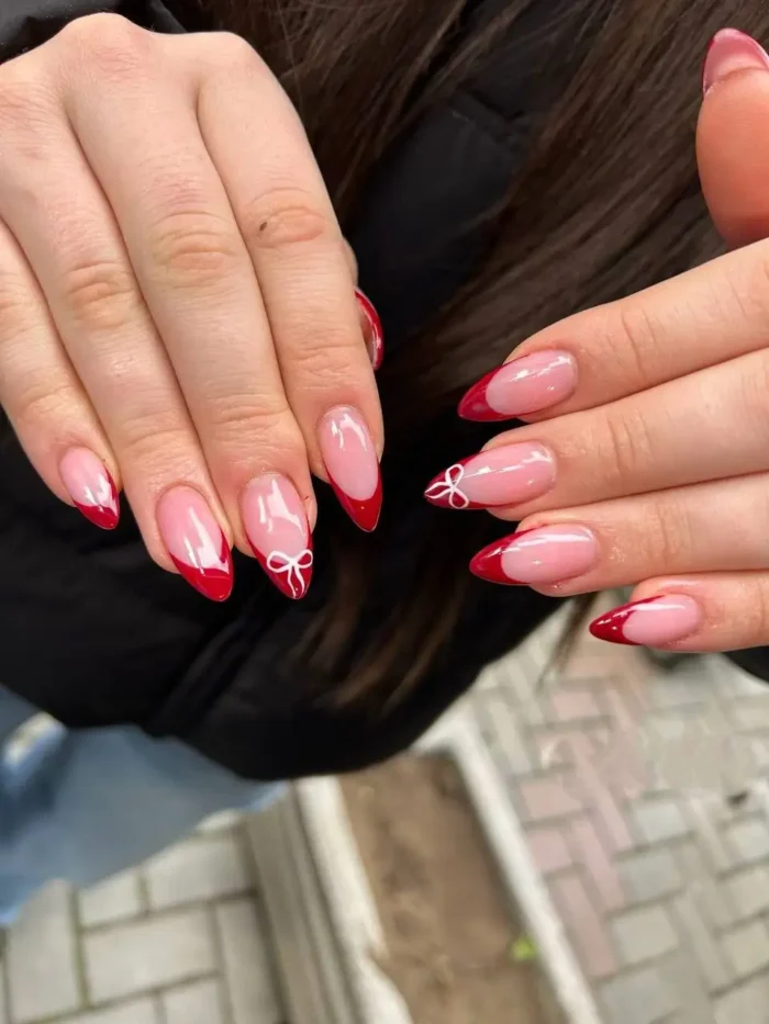 A classic red French tip manicure on almond nails with delicate white bow accents.