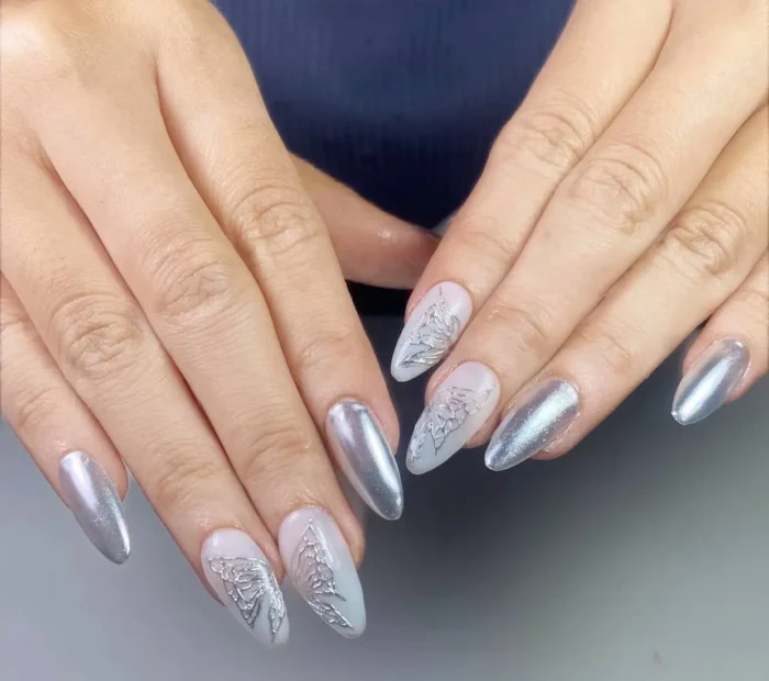 Almond nails featuring pearlescent silver chrome and a milky base with intricate, dimensional silver butterfly wing designs.