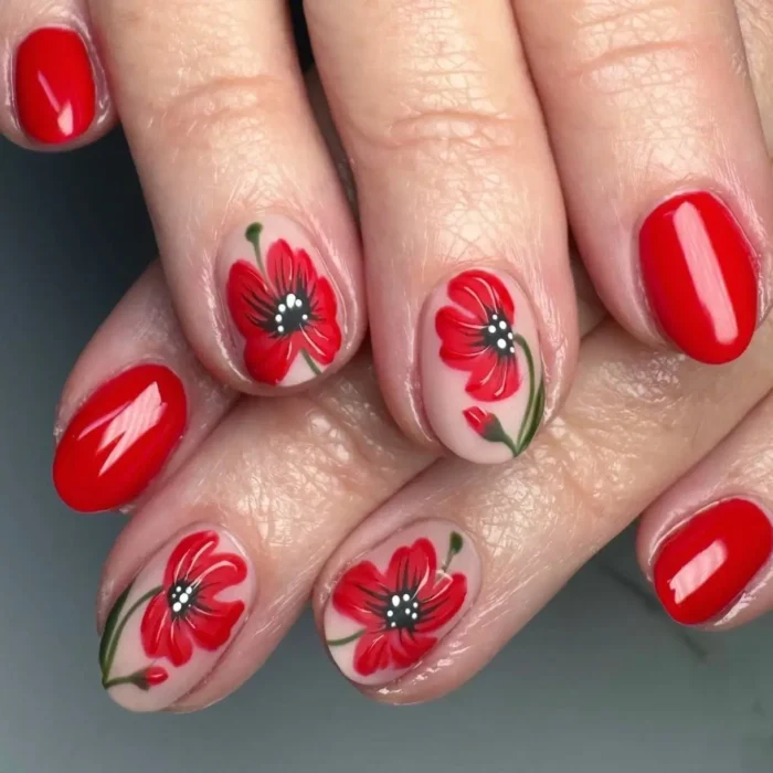 Short, oval-shaped nails with a mix of solid glossy red polish and accent nails with hand-painted red poppy-style flowers.