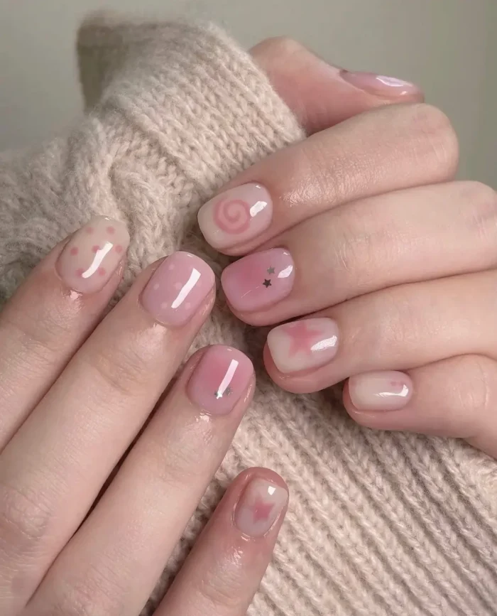 Short rounded nails with a sheer pink base featuring soft pink and white cloudy effects, a pink swirl, and tiny star glitter accents.