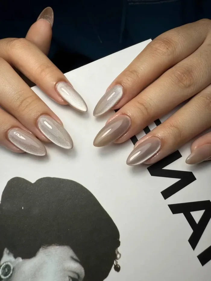 Long almond nails showing a contrast between solid taupe crème polish and pearlescent silver cat-eye effect polish.