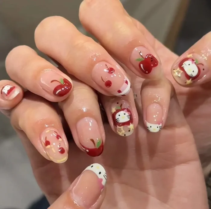 A charming and cute themed manicure on oval nails combining lucky cat characters, juicy red apples, and sweet cherry designs.