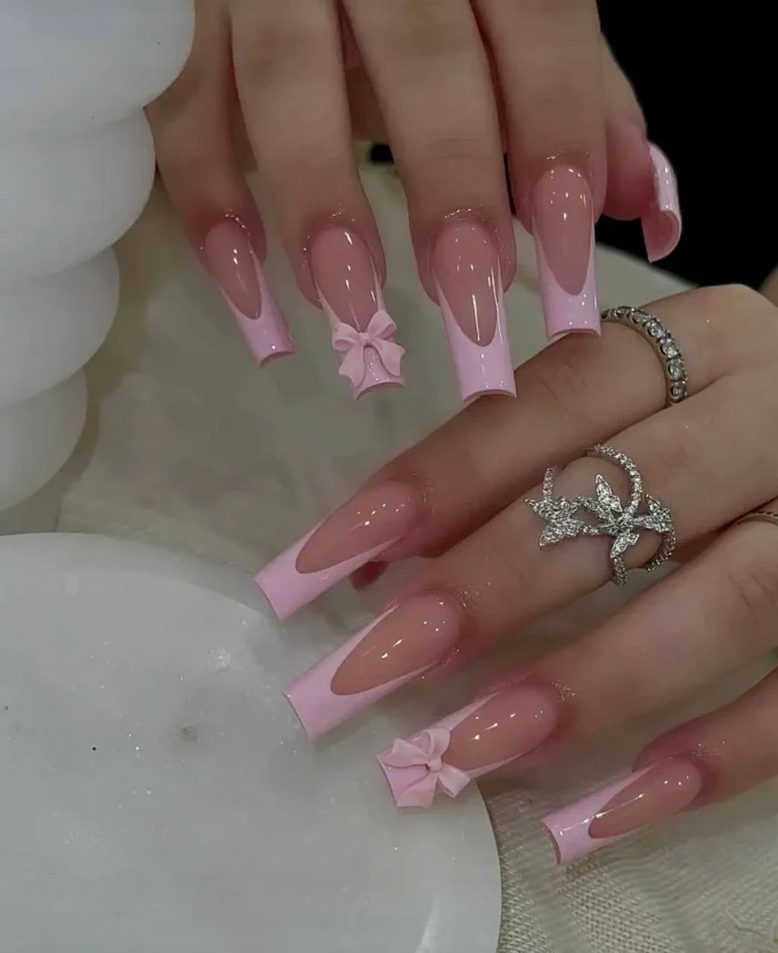 Long square nails with sharp V-shaped baby pink French tips, adorned with matching 3D pink bow accents.