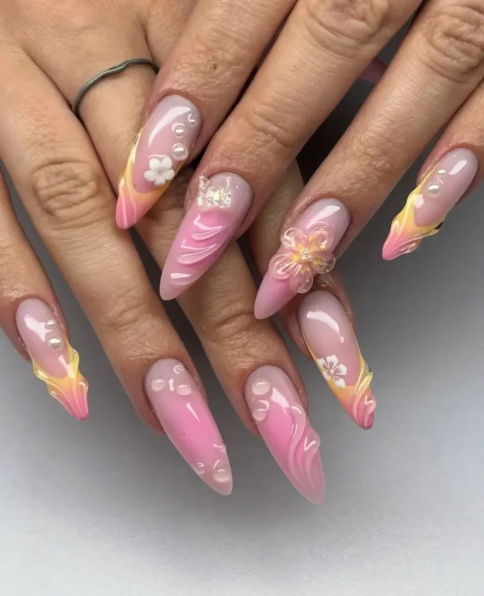 Long stiletto nails with a whimsical summer design, featuring soft pink and yellow ombre tips, 3D swirls, tiny flowers, and pearls.