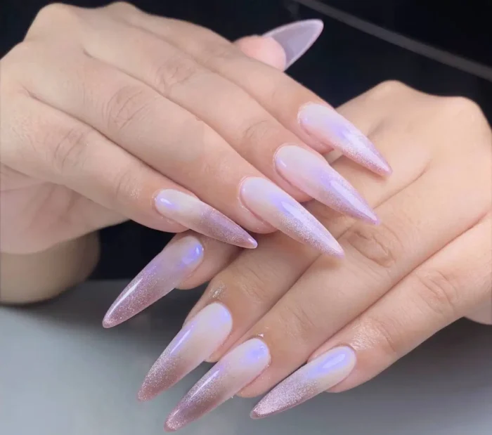 Long stiletto nails featuring a milky base with a soft lavender aura effect blending into a rosy pink glitter gradient at the tips.