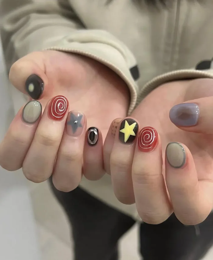 Short rounded nails with a mixed abstract design featuring graphic symbols like swirls, stars, and eyes, plus outlined French tips in muted colors.