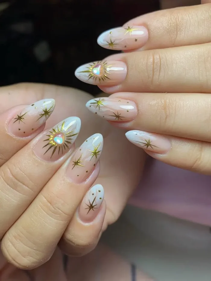 A celestial nail art design on almond nails, featuring delicate gold suns, moons, and stars on a milky white base.
