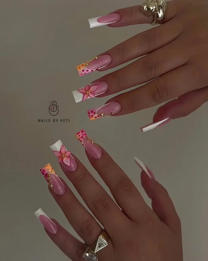 Long square nails with a modern French manicure, featuring pink 3D flowers, colorful dotted tip patterns, and gold chain accents.