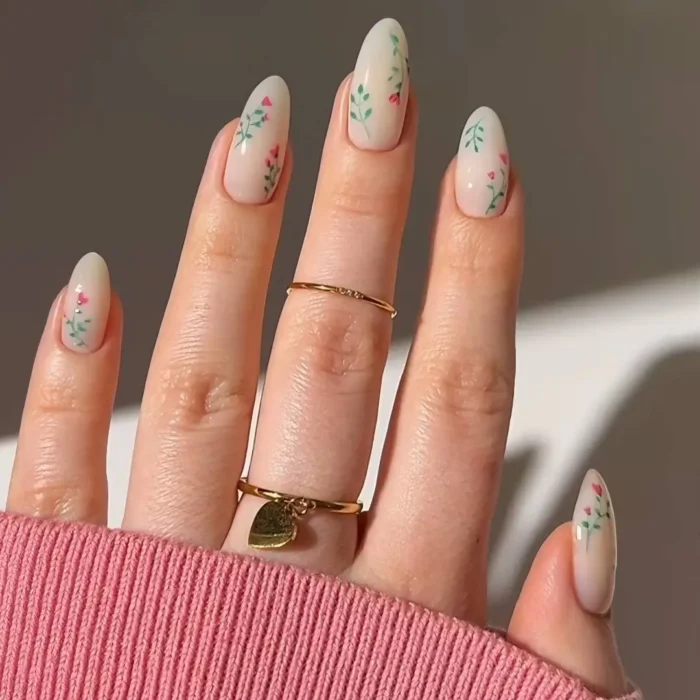Almond-shaped nails with a milky nude base adorned with delicate hand-painted pink flower buds on fine green vines.