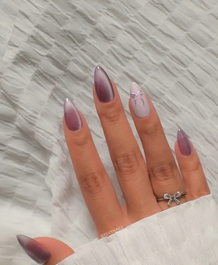Almond-shaped nails in shimmering mauve with a subtle cat-eye effect and a delicate white bow accent on the ring finger.