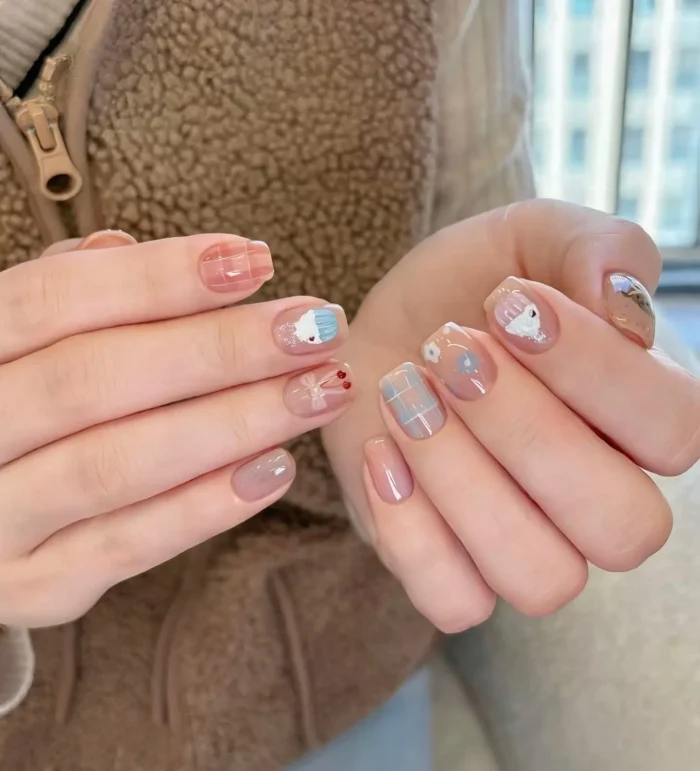 Short rounded nails with a mixed design including coral and blue plaid patterns, cute character illustrations, an abstract swirl, and solid mauve polish.