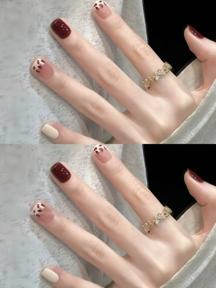 Short square nails with a mixed design: solid deep burgundy, creamy off-white, and sheer nude nails with clusters of tiny brownish-red dots near the cuticles.
