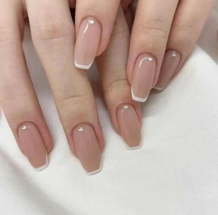 Coffin shaped nails with nude base, thin white micro French tips, and a single small crystal accent near the cuticle.