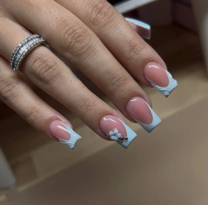 Medium-long square nails showcasing a soft powder blue French tip with a uniquely textured, cloud-like ruffled smile line, accented with a small white 3D flower and rhinestone details.