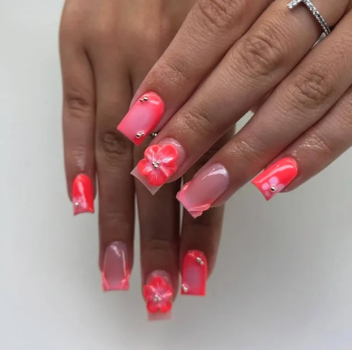 Short square nails with a vibrant coral-pink summer design, featuring ombre, unique framed sheer sections, and sweet 3D flowers.