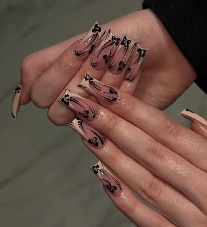 Long coffin-shaped nails with a chic nude beige French tip, adorned with intricate hand-painted black designs including filigree, abstract florals, and delicate dot work.