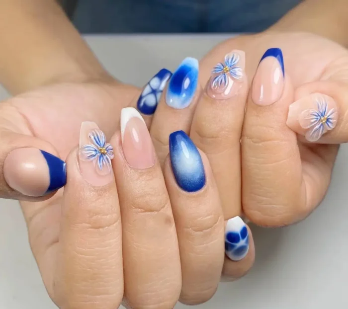 Almond nails with mixed designs in royal blue and white, including French tips, aura effects, abstract patterns, and 3D floral accents.