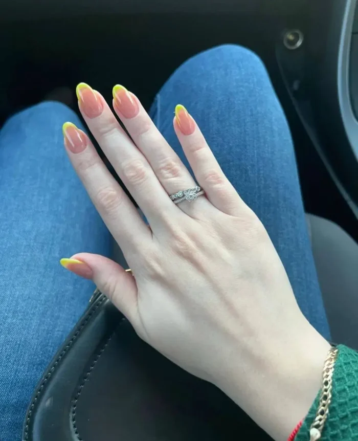 Long almond shaped nails with a sheer nude base and vibrant bright yellow French tips.