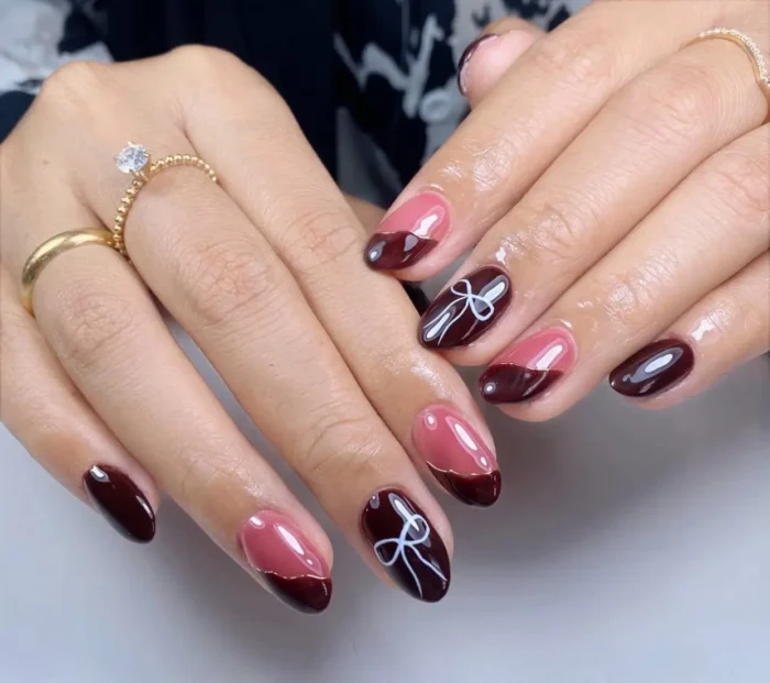 Oval nails featuring deep oxblood and dusty pink polish, with designs including curved French tips with gold lines and white bow outlines.
