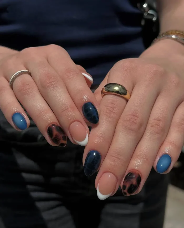 Short rounded nails with a mixed design including tortoise shell print, sheer blue jelly polish, textured navy blue, and a classic white French tip.
