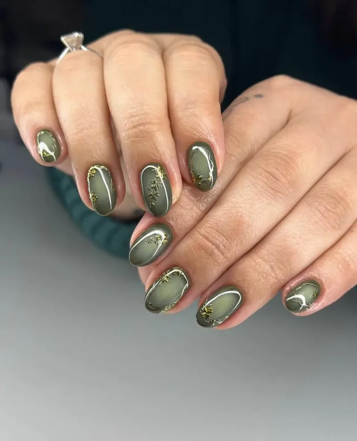 Medium oval nails with deep olive green cat-eye polish base, accented with delicate gold snowflake designs.