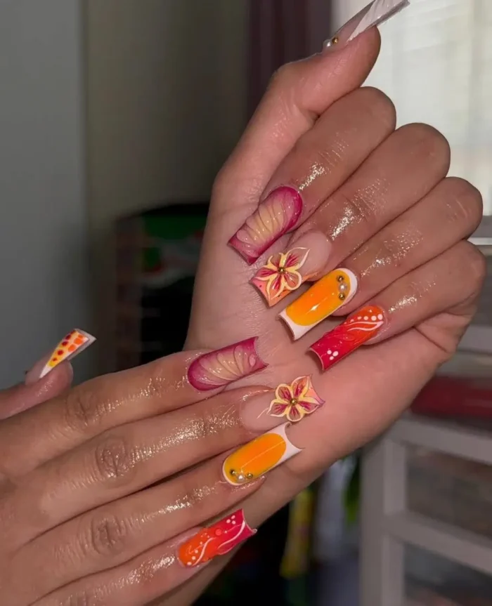 Long square nails with a vibrant summer design of sunset-hued abstract art, modern French tips, and delicate 3D flowers.
