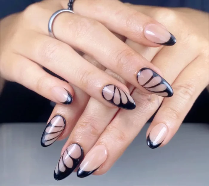 Almond nails with a sheer nude base featuring graphic black outlines creating an abstract butterfly wing design, plus simple black French tips.