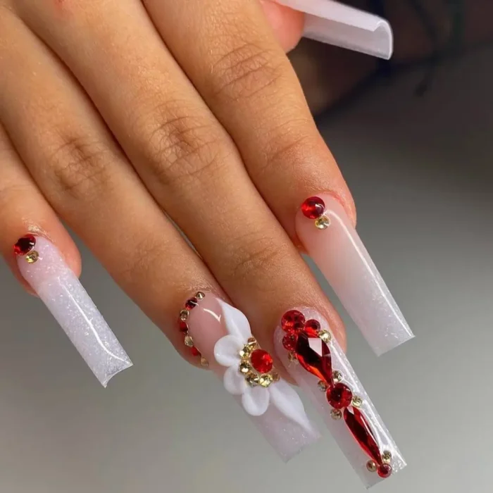 Long coffin nails with a milky white base, featuring a 3D white flower and bold red gemstone embellishments.