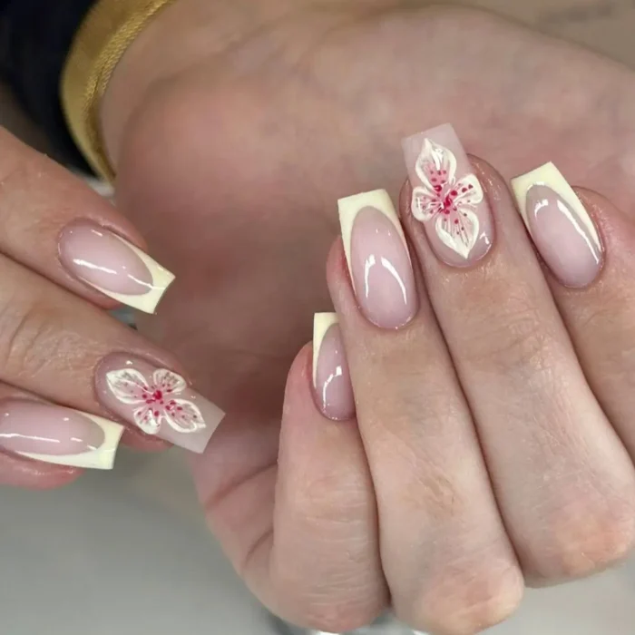 A deep French manicure with pale yellow tips and a detailed 3D white and pink speckled orchid on the accent nail.