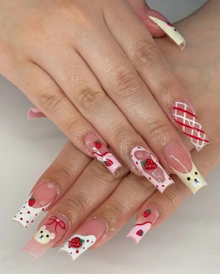 Playful long square nails with a picnic theme, featuring painted strawberries with white polka dots, cute teddy bear faces with red bows, and red and white gingham patterns.