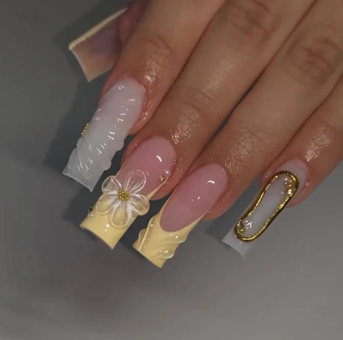 Elegant long square nails showcasing pastel yellow sculpted French tips, a translucent 3D flower with a gold center, abstract gold liquid-metal designs, and subtle pearl accents.