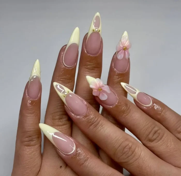 A set of long stiletto nails with a deep butter yellow French manicure, accented with 3D flowers and pearls.