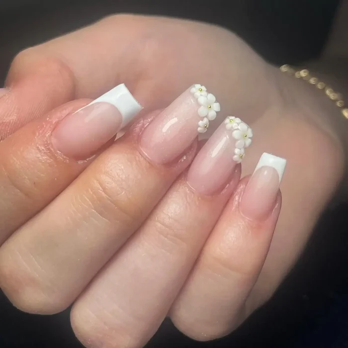 Square-shaped nails with a classic white French manicure, accented by a cascade of small 3D white flowers with gold bead centers.
