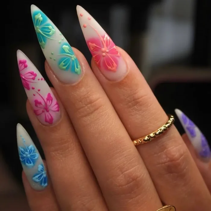 Long stiletto nails with a matte base, adorned with vibrant pink, blue, and purple etched-style flower designs.
