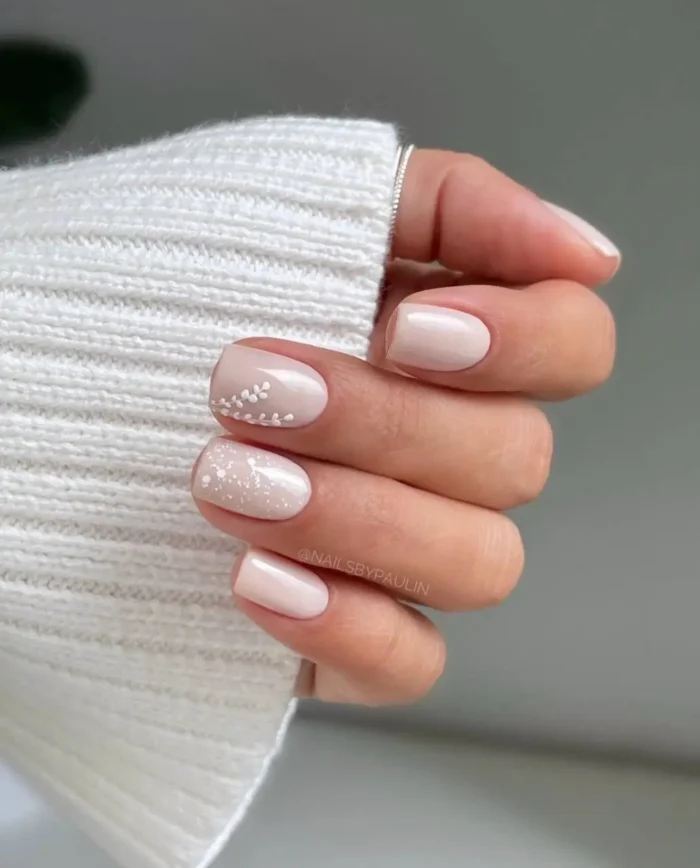 Neutral, sheer-toned nails with delicate white botanical or floral accents, conveying an elegant and subtle design.