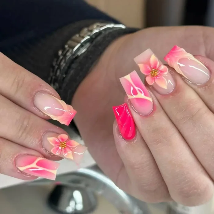 A long square manicure with mismatched designs, including hot pink airbrush art and 3D pink and yellow ombré flowers.