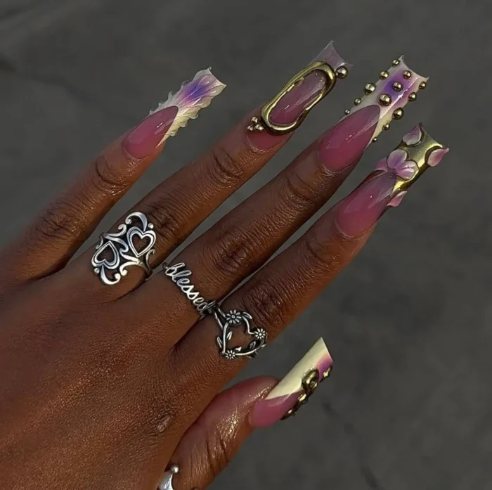 Long sculpted magenta jelly nails with antique gold 3D embellishments, floral details, and iridescent wispy tips.