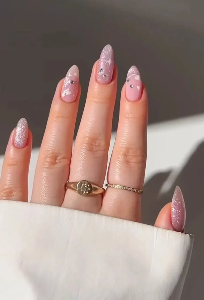 A whimsical and cute nail design with fluffy cartoon clouds on a creamy pink base and sparkling glitter accent nails.