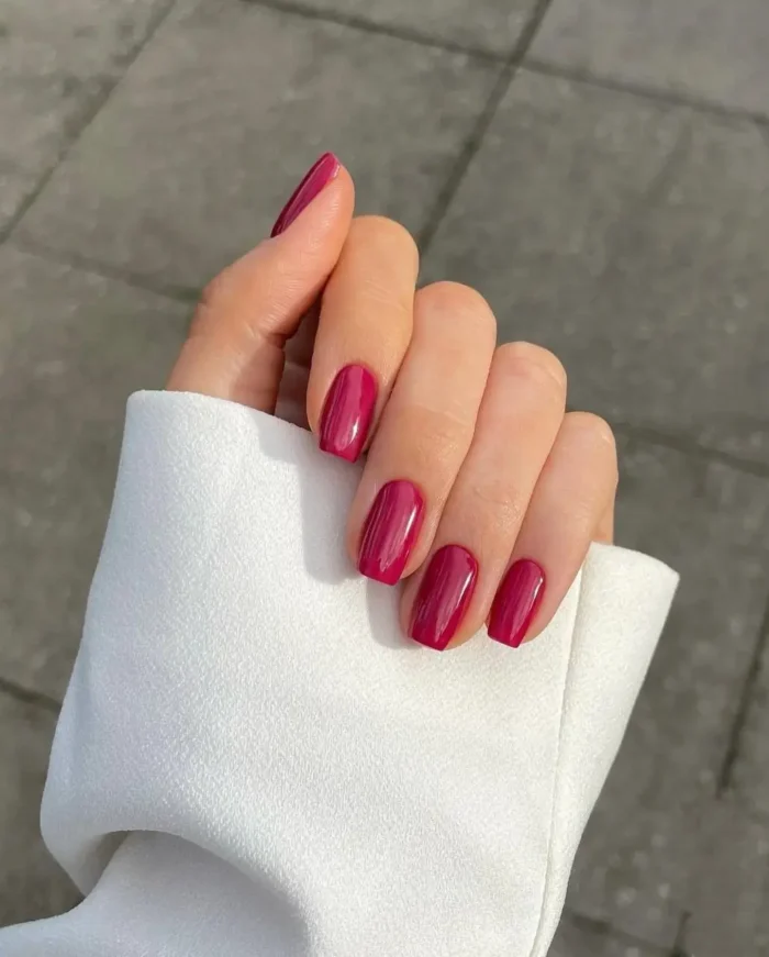 Short, glossy nails painted in a rich, vibrant berry or fuchsia color, showcasing a simple yet bold manicure.