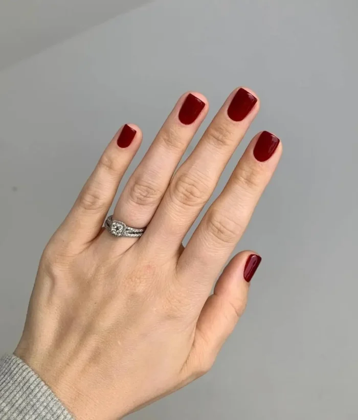 A chic manicure on short square nails painted with a solid, glossy deep burgundy red polish.